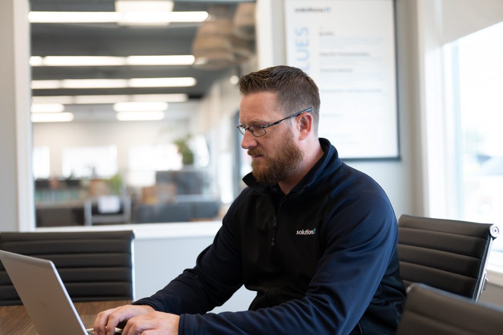 Randy working on a laptop at a meeting table in the SolutionsIT office.